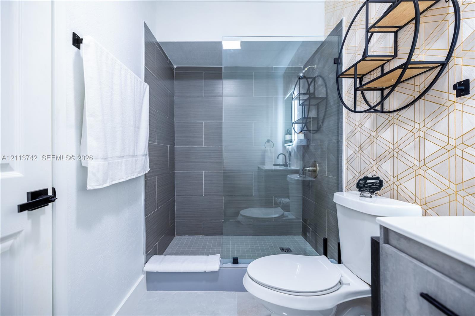 Walk-in shower featuring gray horizontal tile surround, glass enclosure, and modern metal hardware, complemented by geometric patterned wall tile