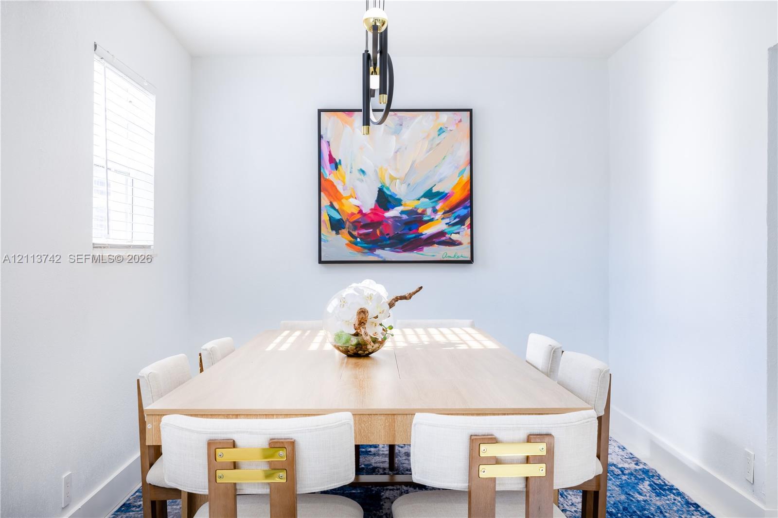 Dining area featuring neutral wall paint, modern multi-tiered linear pendant lighting, and a single window with horizontal blinds