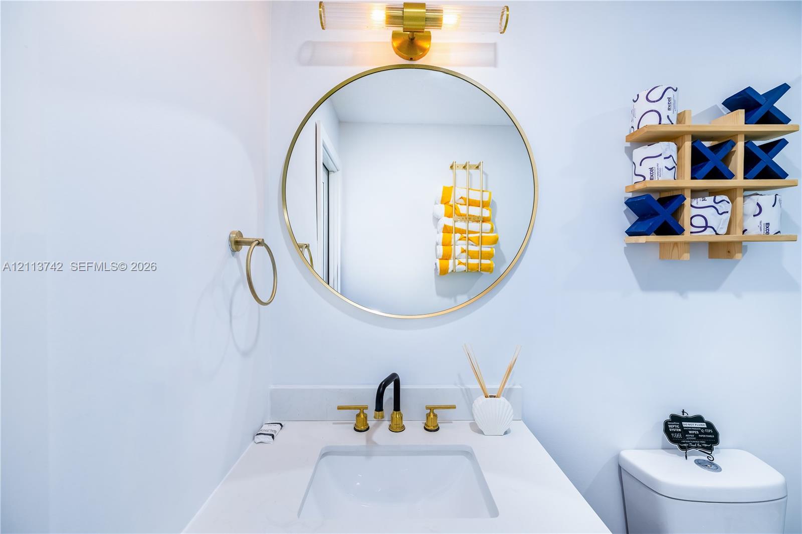 Bathroom vanity featuring a quartz countertop, rectangular undermount sink, brass finish widespread faucet, round brass-framed mirror, and a linear wall-mounted light fixture
