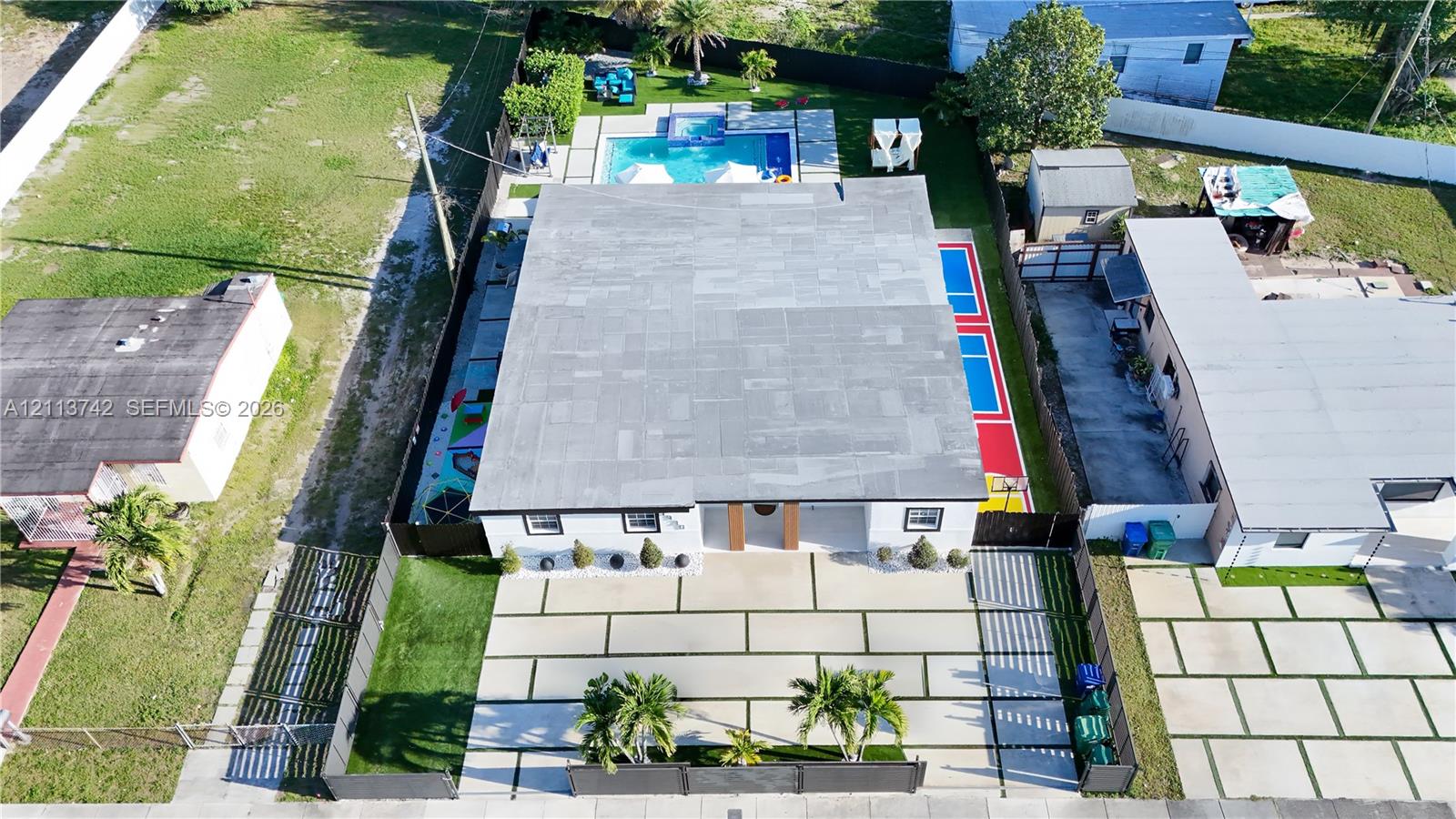 Aerial perspective featuring a structured concrete driveway with integrated turf ribbons, a rear swimming pool with integrated spa, and a multi-purpose sport court