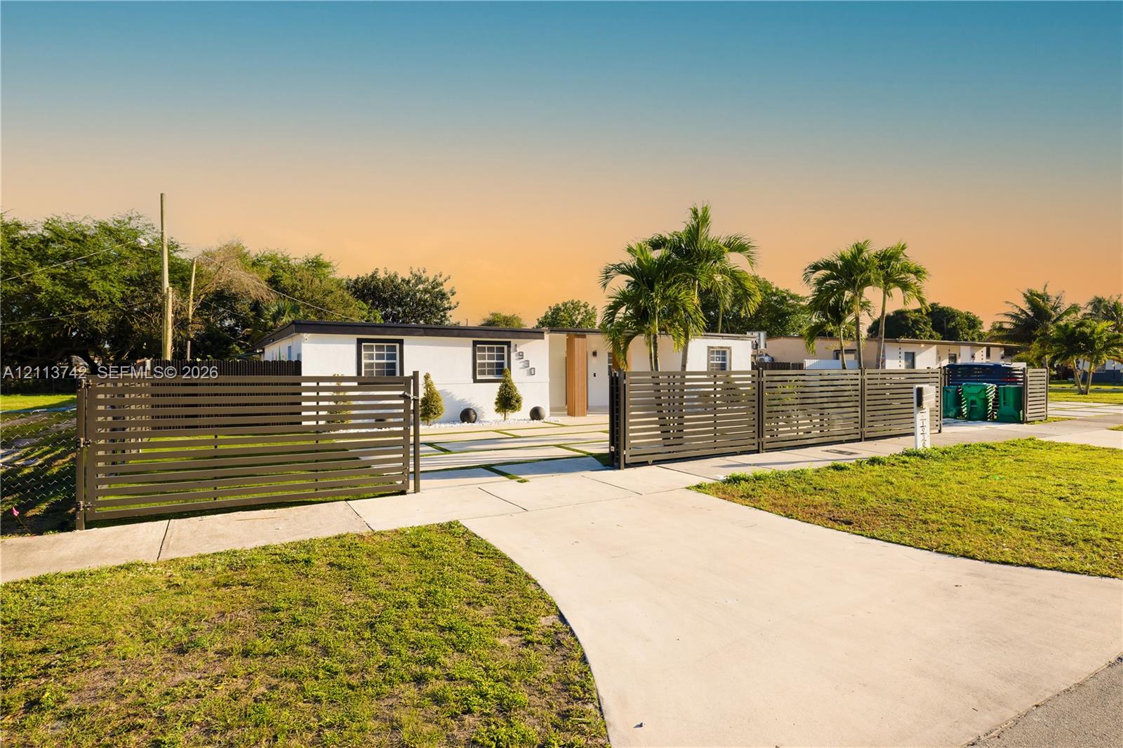 Single-story exterior featuring white stucco finish, horizontal slat privacy fencing, concrete driveway, and palm tree landscaping Single-story exterior featuring white stucco finish, horizontal slat privacy fencing, concrete driveway, and palm tree landscaping