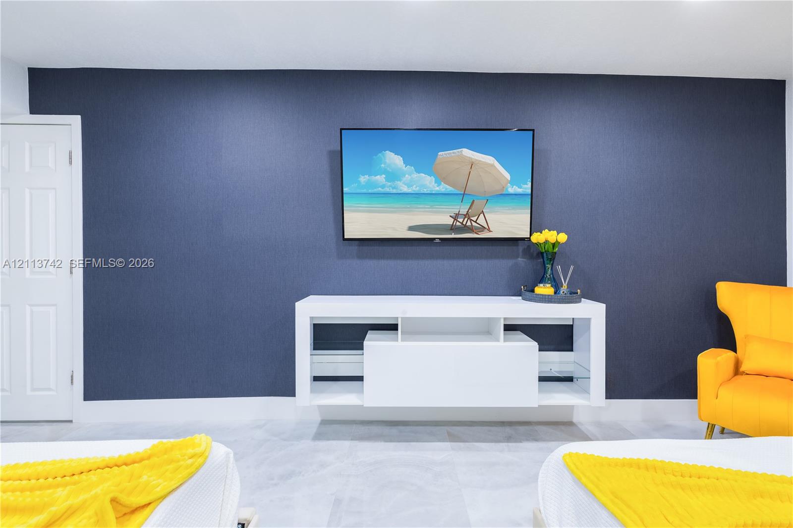 Deep blue accent wall with a wall-mounted television, white built-in media console, and large-format tile flooring