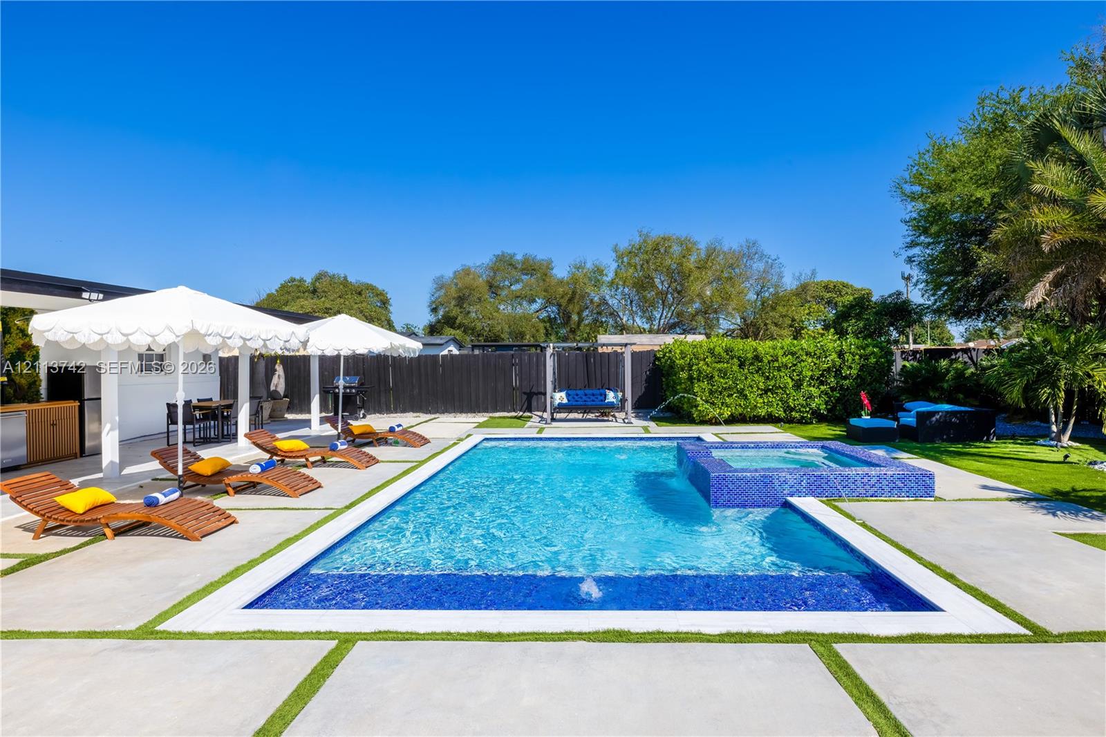 In-ground pool with integrated spa and blue tile finish, surrounded by large-format concrete pavers with artificial turf inlay