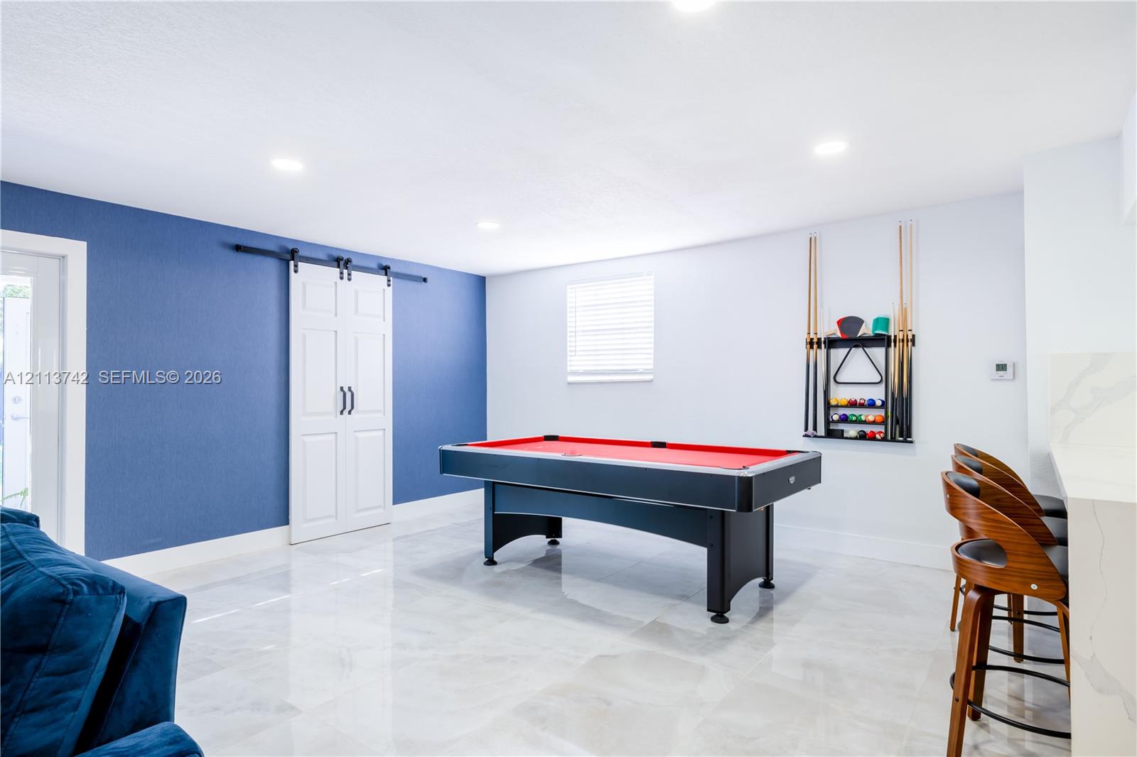 Recessed lighting, large-format tile flooring, blue accent wall, white sliding barn door, and a built-in stone-top bar surface