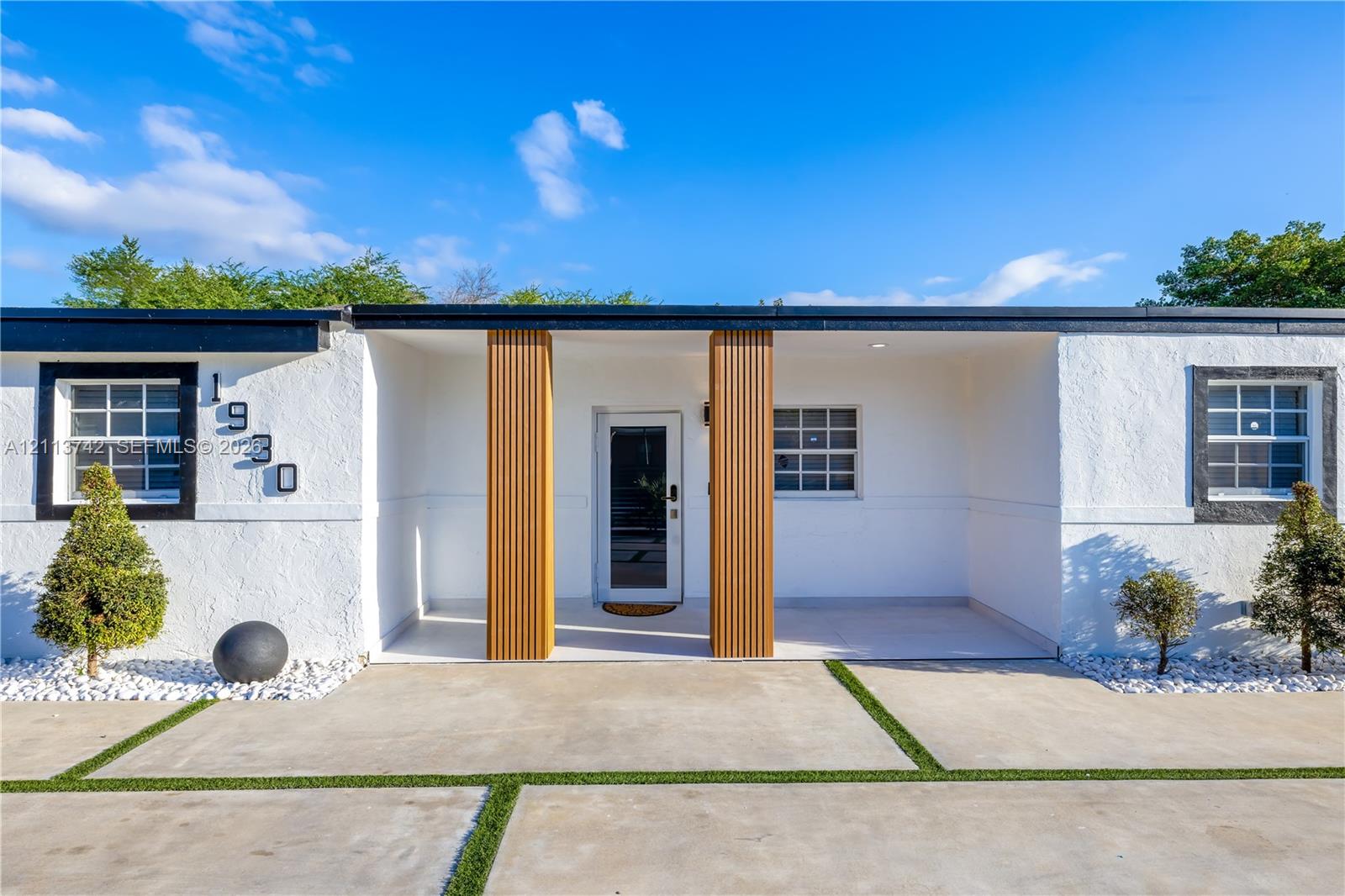 Modern exterior featuring a white stucco facade, a covered entryway with vertical wood-slat columns, and a grid-patterned concrete driveway with integrated turf strips Modern exterior featuring a white stucco facade, a covered entryway with vertical wood-slat columns, and a grid-patterned concrete driveway with integrated turf strips