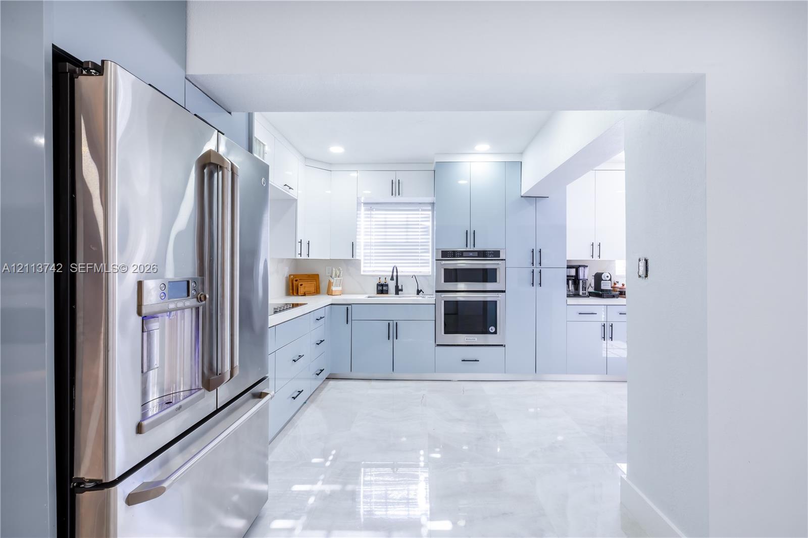 Kitchen featuring light blue custom cabinetry, stainless steel appliances including a built-in double oven and French door refrigerator, white countertops, and polished tile flooring
