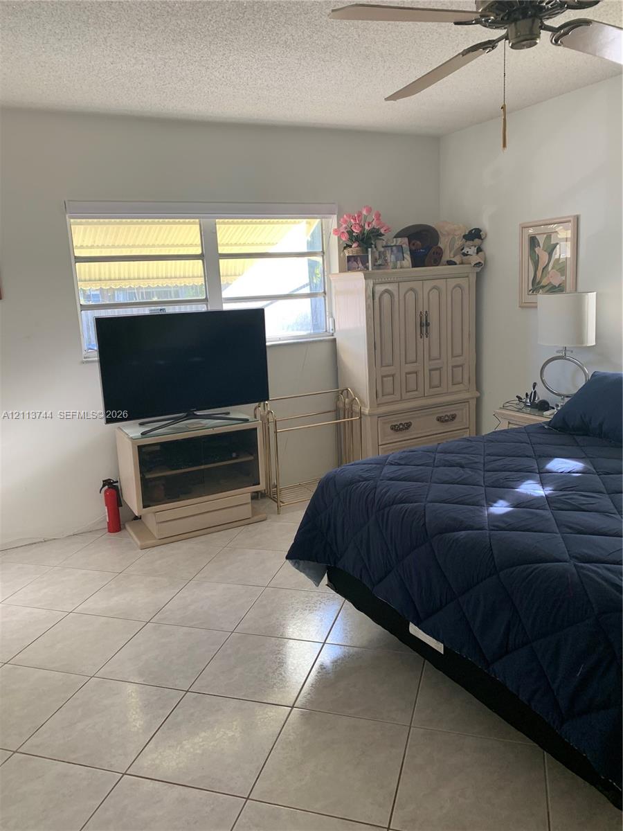 Neutral-toned ceramic tile flooring, horizontal window with white window shade, and ceiling-mounted fan with light fixture