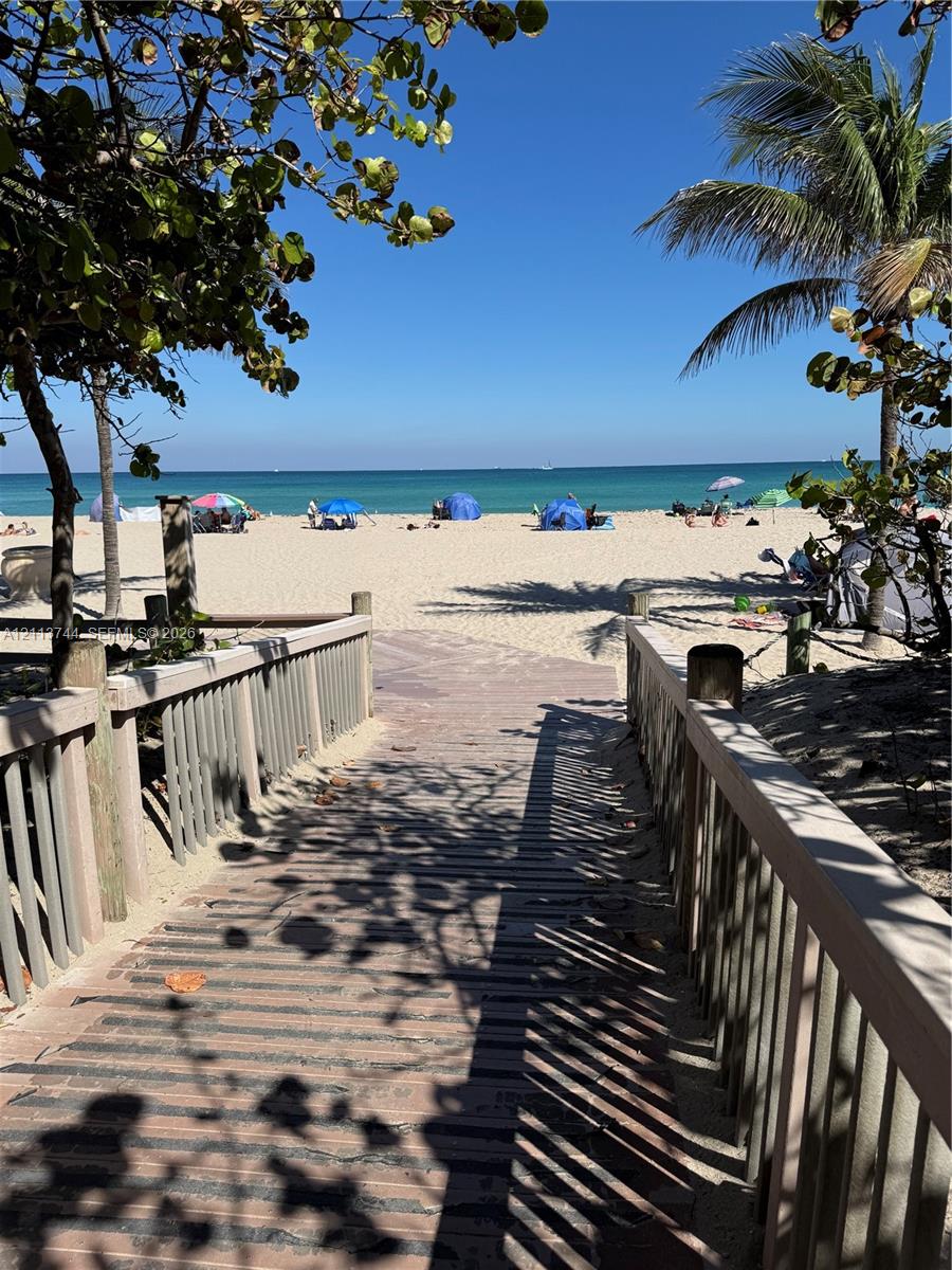 Elevated wooden boardwalk featuring post-and-rail fencing, mature palm trees, and direct sand access to the coastline