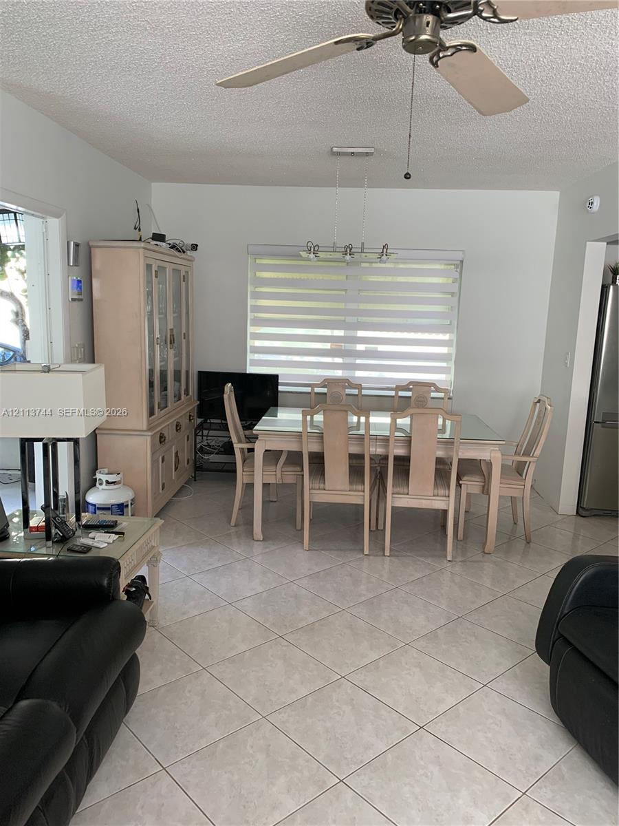 Light-toned ceramic tile flooring, ceiling fan with light kit, and multi-light linear chandelier