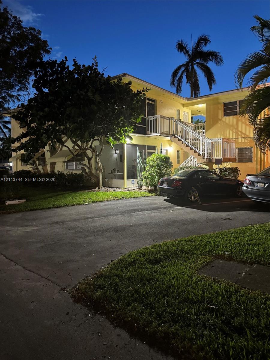 Two-story exterior featuring a screened-in ground-level patio, an elevated balcony with white metal railings, and an asphalt parking area Two-story exterior featuring a screened-in ground-level patio, an elevated balcony with white metal railings, and an asphalt parking area
