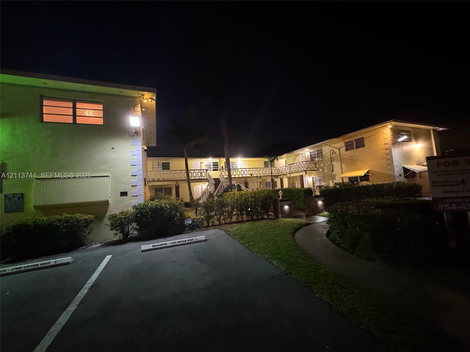 Multi-story exterior featuring masonry construction, a concrete walkway, designated parking spaces, and decorative railing