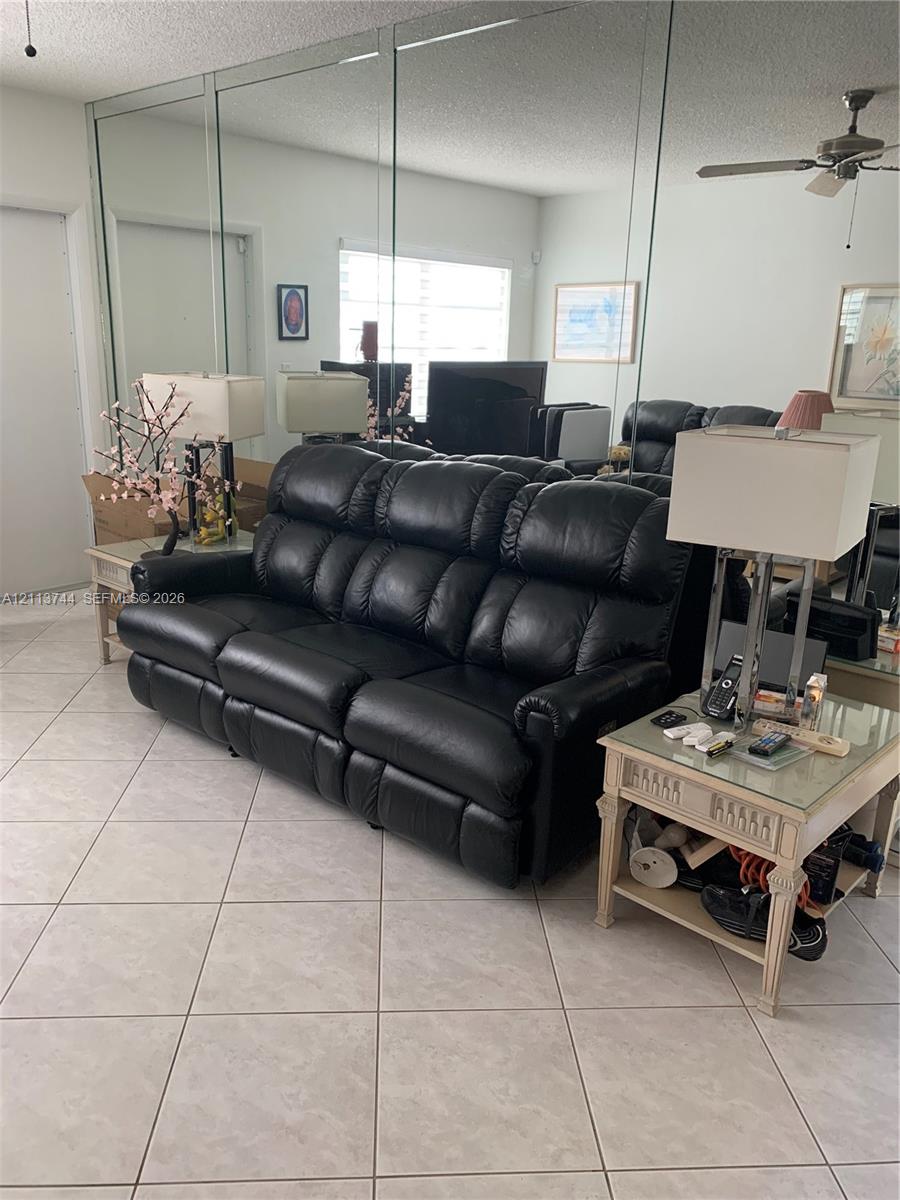 Living area featuring large-format ceramic tile flooring, floor-to-ceiling wall-mounted mirrors, and a ceiling-mounted fan