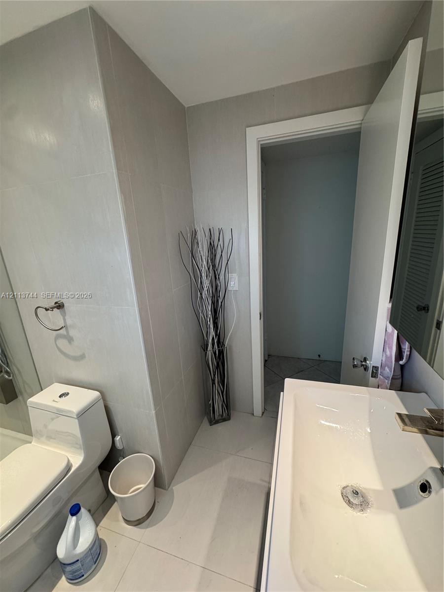 Bathroom featuring large-format wall and floor tiling, a one-piece dual-flush toilet, a white ceramic wall-mounted sink, and a glass-enclosed shower
