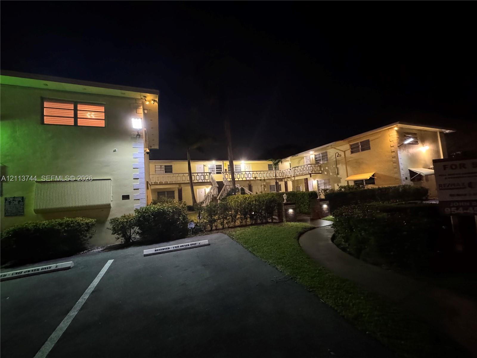Two-story exterior featuring a stucco facade, decorative geometric railings, covered walkways, and paved parking area with designated spaces