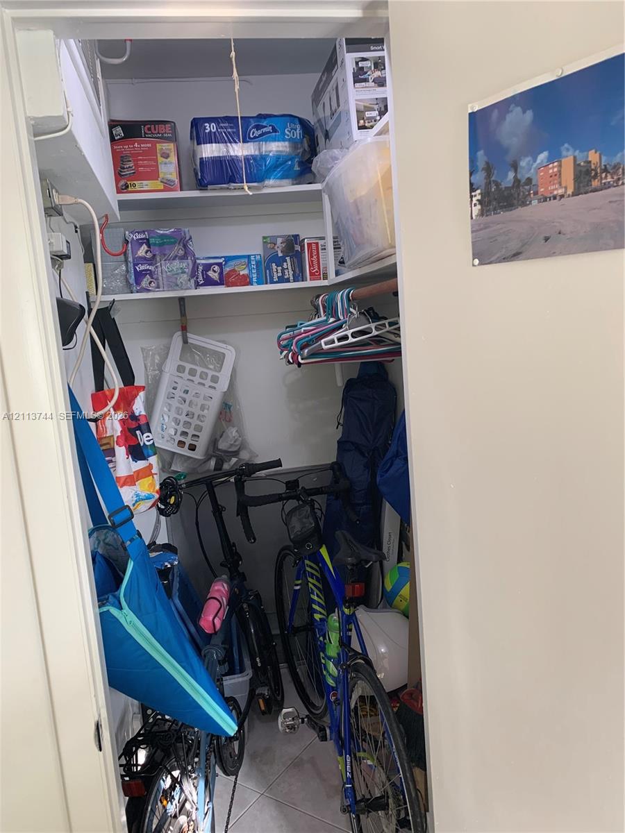 Storage closet featuring two tiers of white fixed shelving and neutral ceramic tile flooring