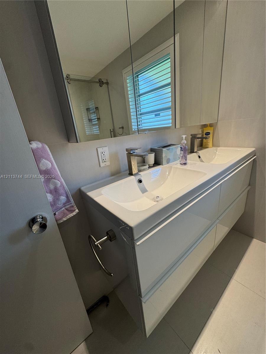 Floating dual-sink vanity featuring a high-gloss finish, integrated basins, and minimalist chrome faucets, complemented by a wide medicine cabinet and large-format floor tiling