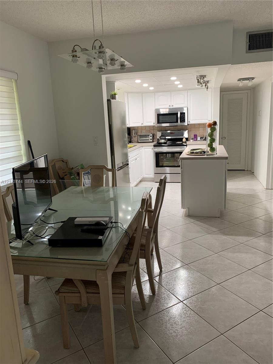 Kitchen featuring white cabinetry, stainless steel appliances, an integrated island, recessed lighting, and tile flooring
