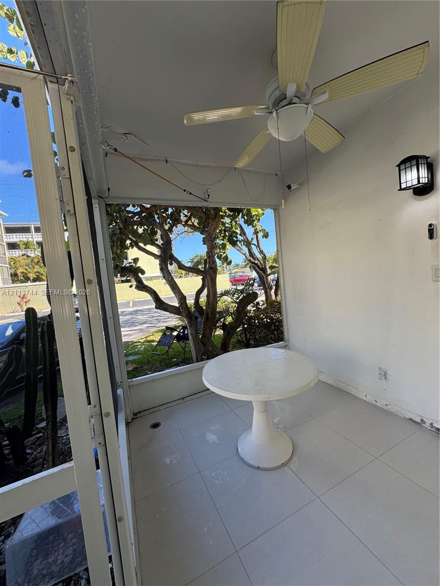 Screened-in porch featuring large-format tile flooring, a ceiling fan with integrated lighting, and a wall-mounted lantern-style exterior fixture