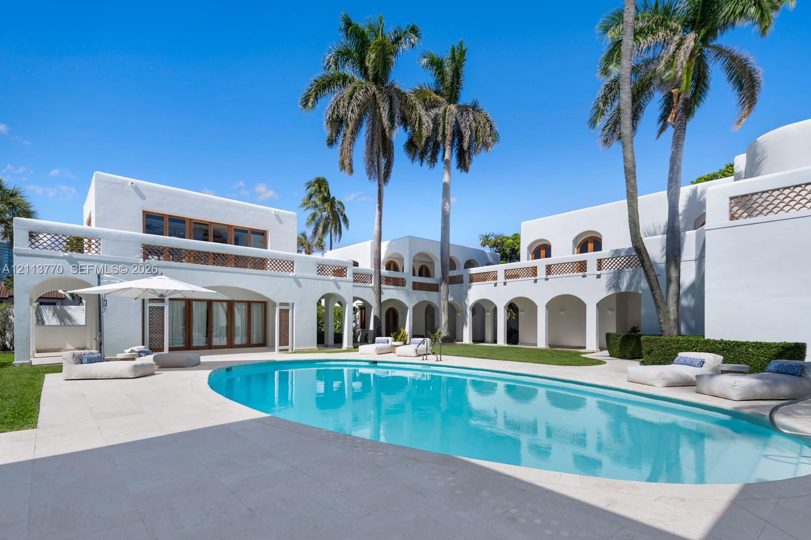 Stucco exterior featuring arched covered loggias, second-story balconies with decorative latticework, oval swimming pool, and stone-finished patio