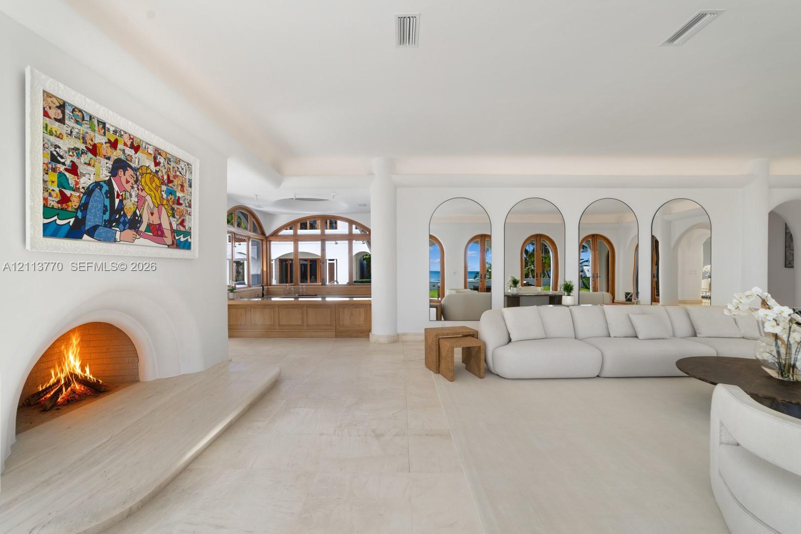 Open-concept living space featuring stone flooring, a recessed arched fireplace with an extended stone hearth, and floor-to-ceiling arched mirrors