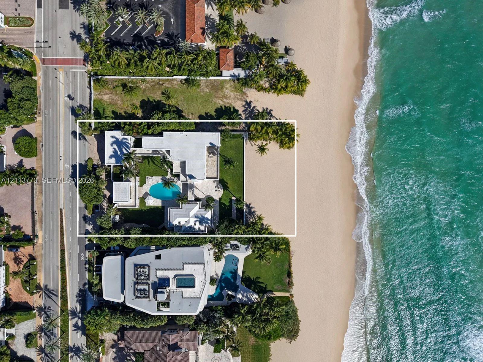 Direct oceanfront property featuring a private swimming pool, expansive paved patio, manicured lawn, and mature perimeter landscaping