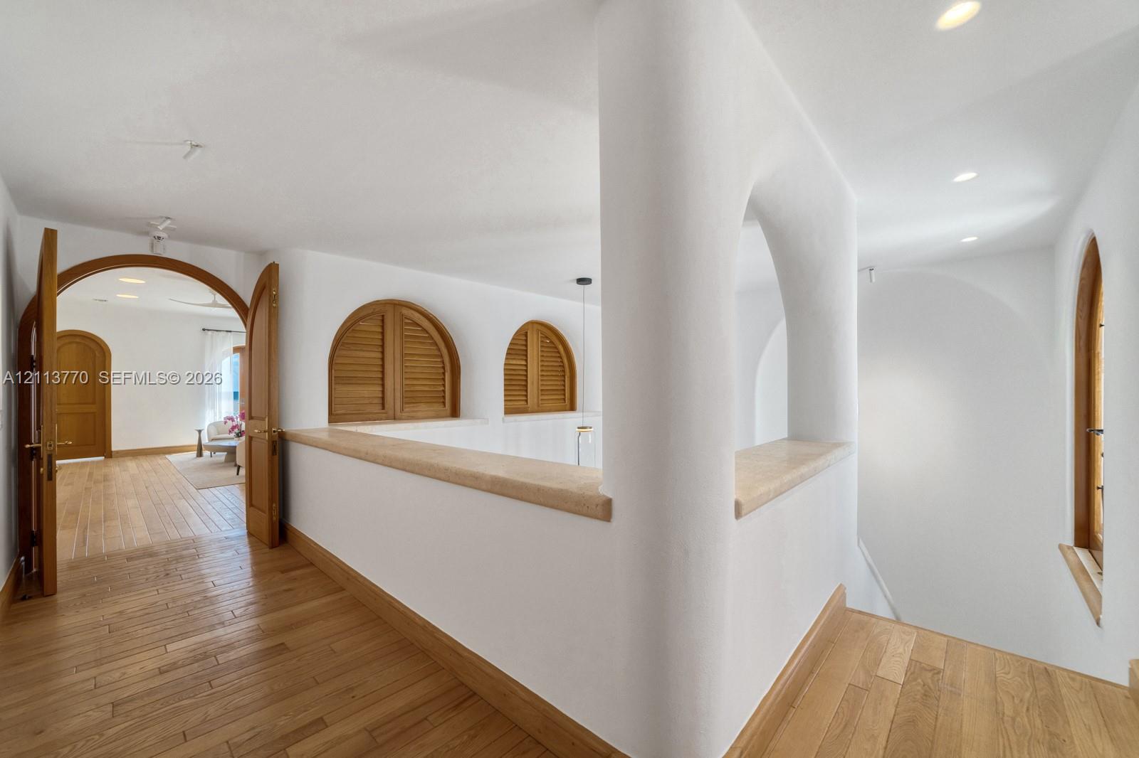 Arched architectural openings, smooth plaster wall finishes, wood-finish flooring, recessed lighting, and wooden louvered shutters