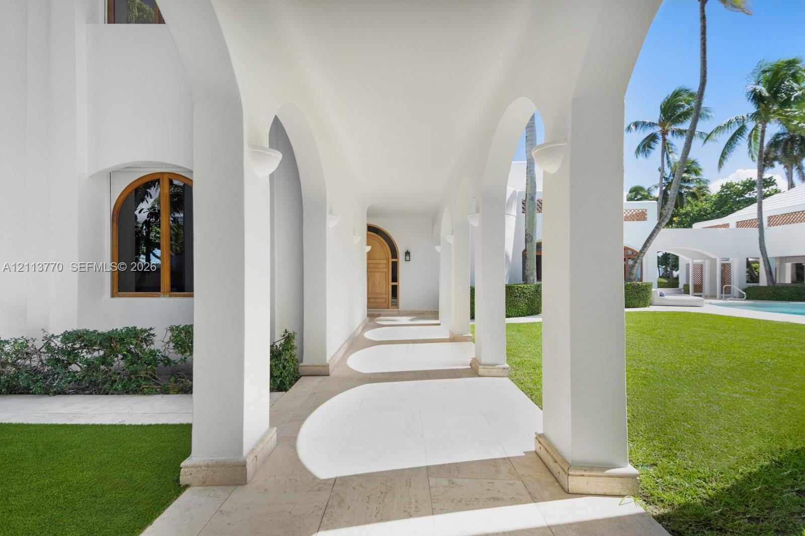 Covered arcade featuring rhythmic structural arches, natural stone flooring, and built-in wall-mounted sconces