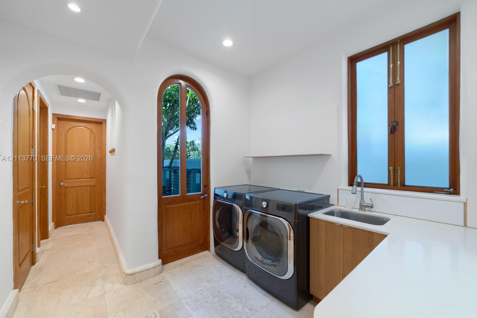 Laundry area featuring stone tile flooring, an arched glass-paneled door, custom wood cabinetry with a sink, and a solid surface countertop