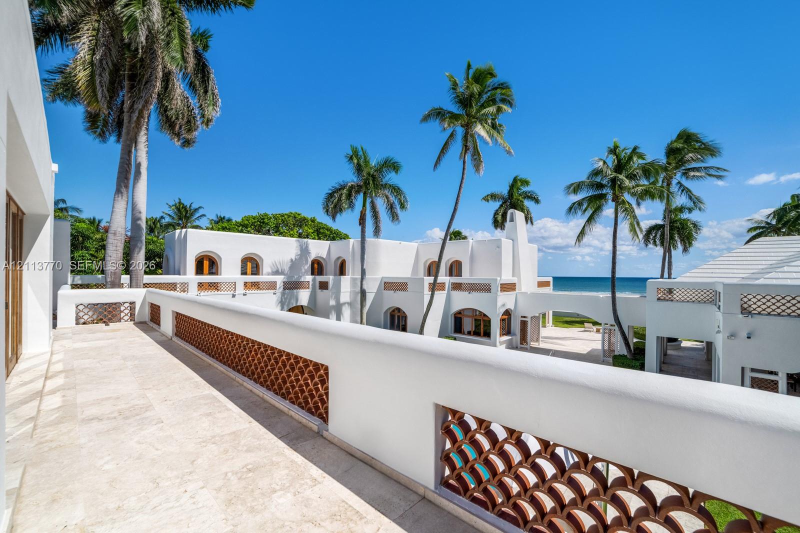 Second-story stone terrace featuring decorative terracotta latticework railings, stucco exterior walls, arched architectural detailing, and ocean surroundings