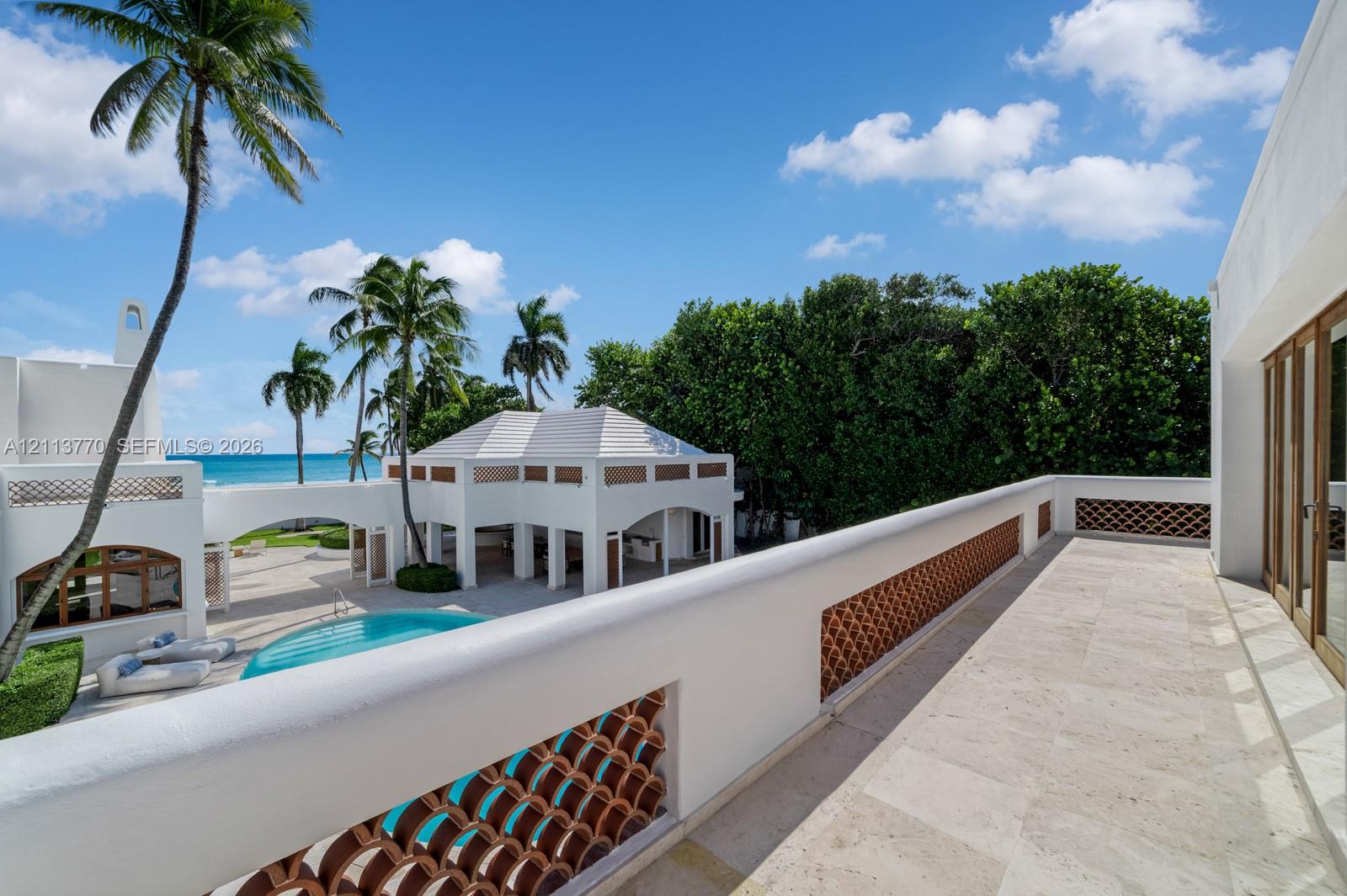 Second-story balcony featuring stone flooring and decorative terracotta balustrades, overlooking an outdoor pool area with a covered pavilion and tropical landscaping