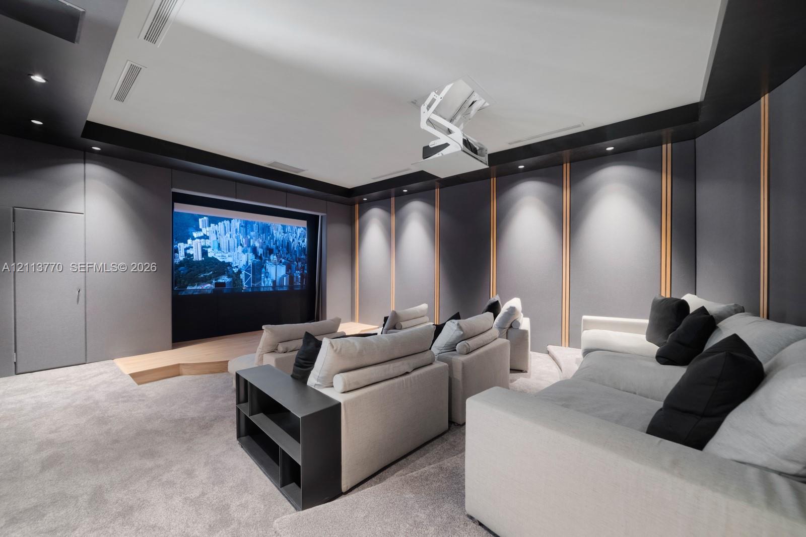 Media room featuring tiered flooring, custom acoustic wall paneling with integrated wood slats, recessed ceiling lighting, and a mounted overhead projector