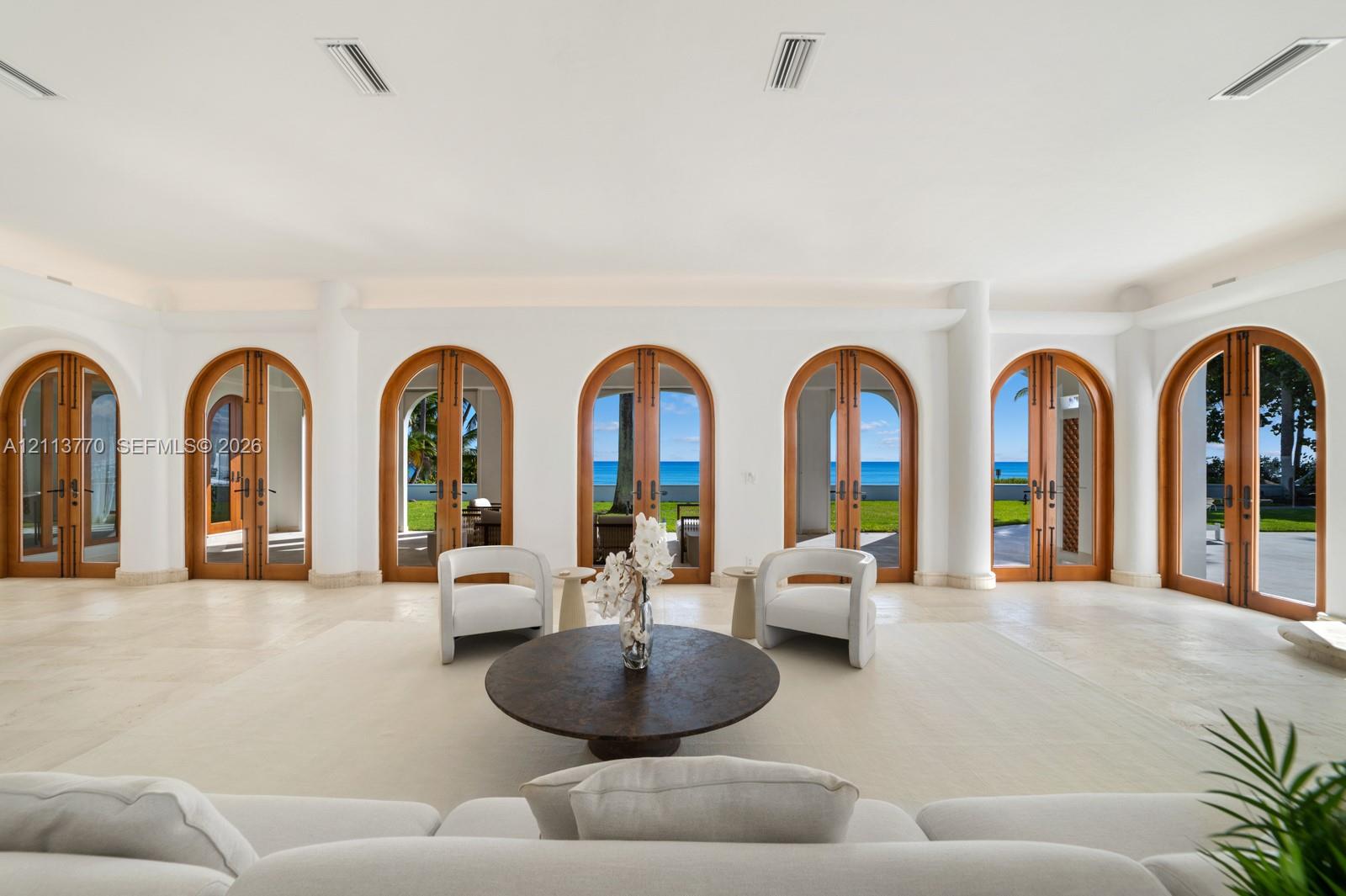 Living area featuring arched wood-framed glass double doors, large-format stone flooring, structural columns, and recessed ceiling lighting