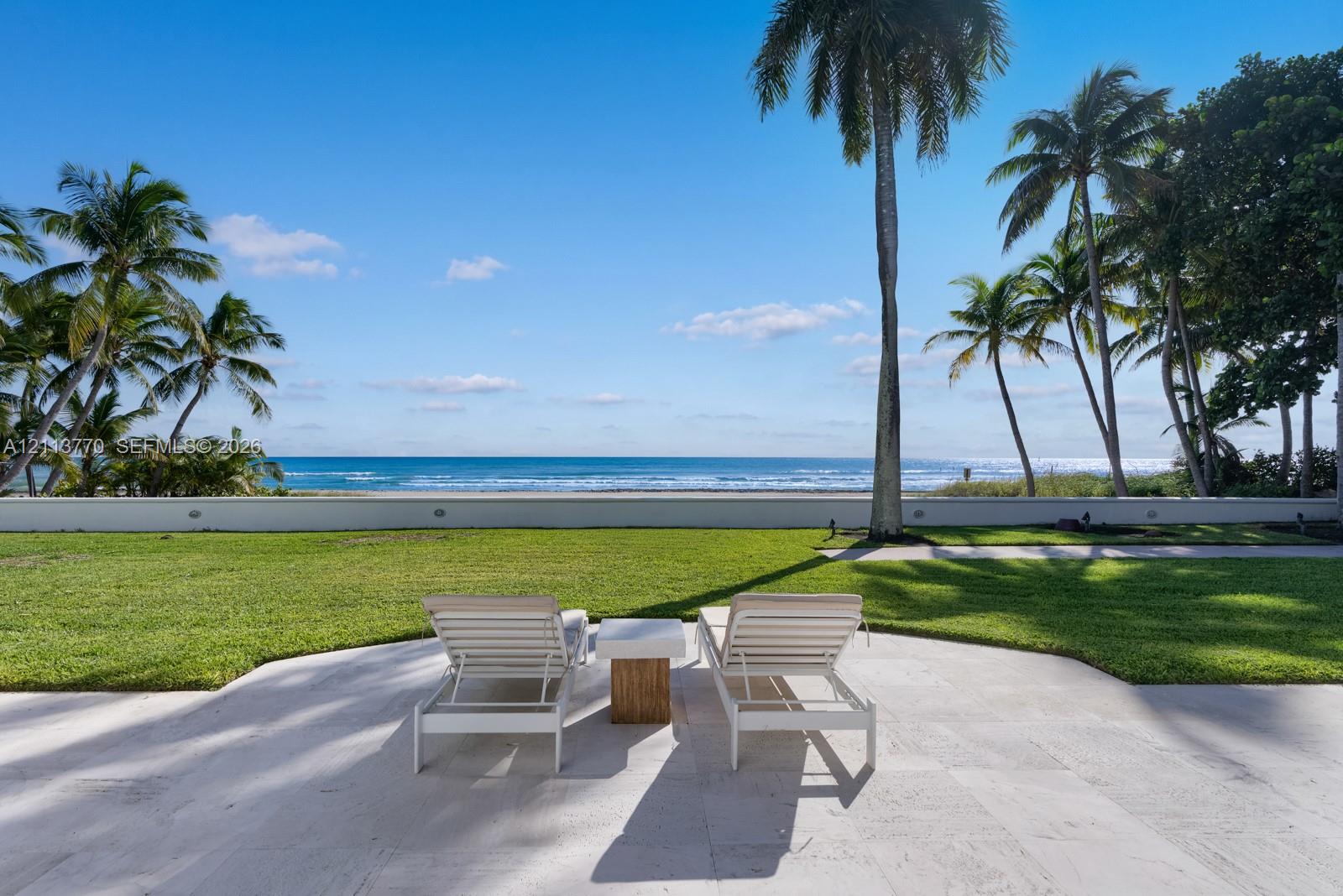Stone-paved patio featuring a manicured lawn, perimeter masonry wall, and oceanfront exposure