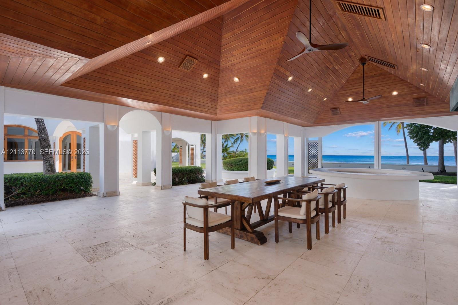 Covered outdoor pavilion featuring a vaulted wood-plank ceiling, recessed lighting, ceiling fans, stone flooring, and a built-in circular masonry counter