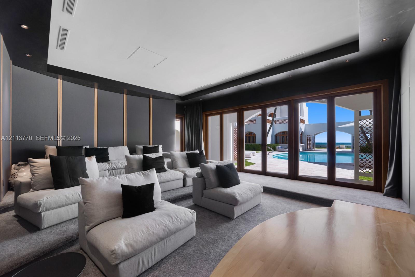 Media room featuring tiered flooring, decorative wall paneling with metallic accents, recessed ceiling lighting, and expansive multi-panel wood-framed glass doors