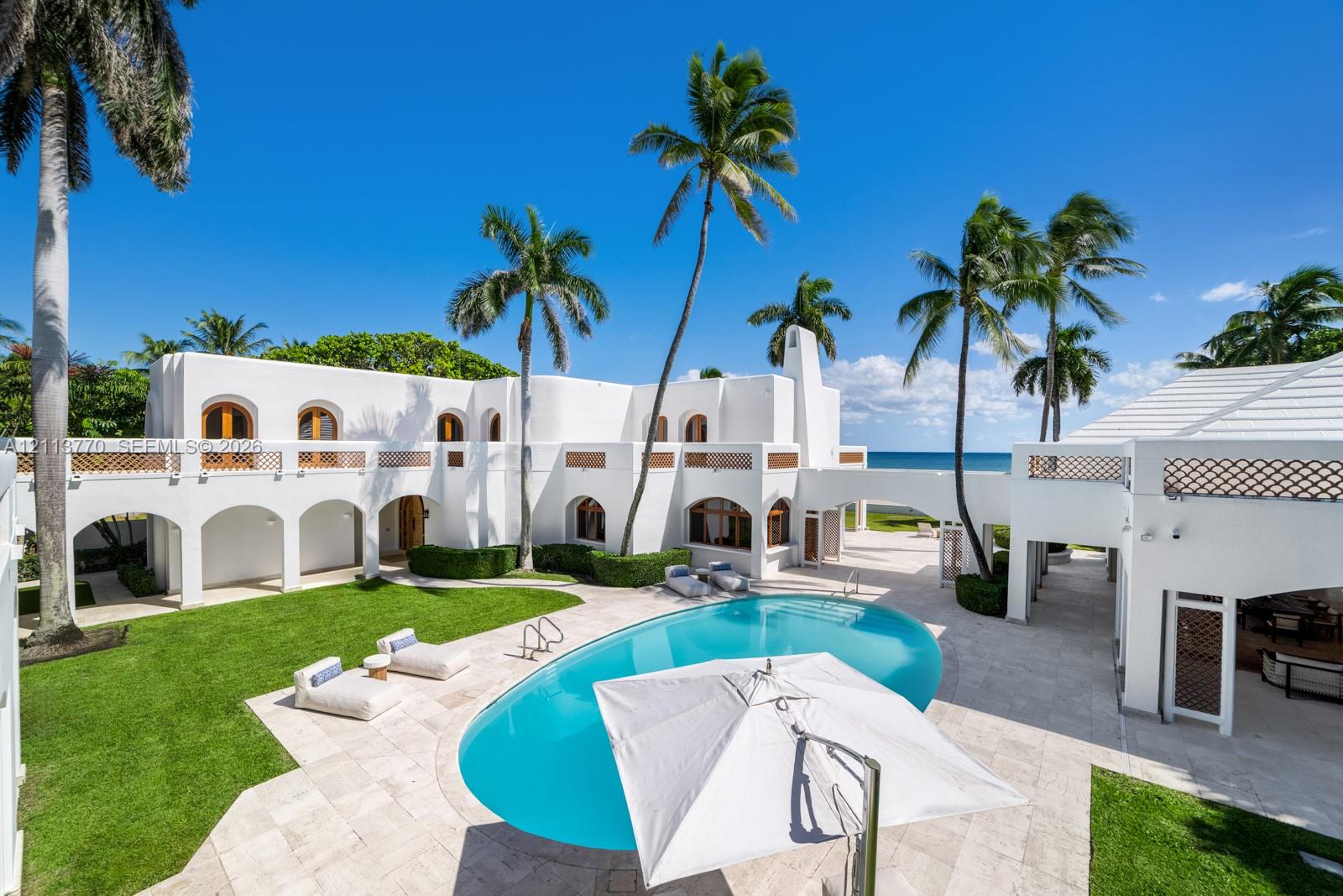 Mediterranean-style exterior featuring arched colonnades, white stucco finish, second-story decorative lattice railings, a private swimming pool with stone decking, and mature palm trees