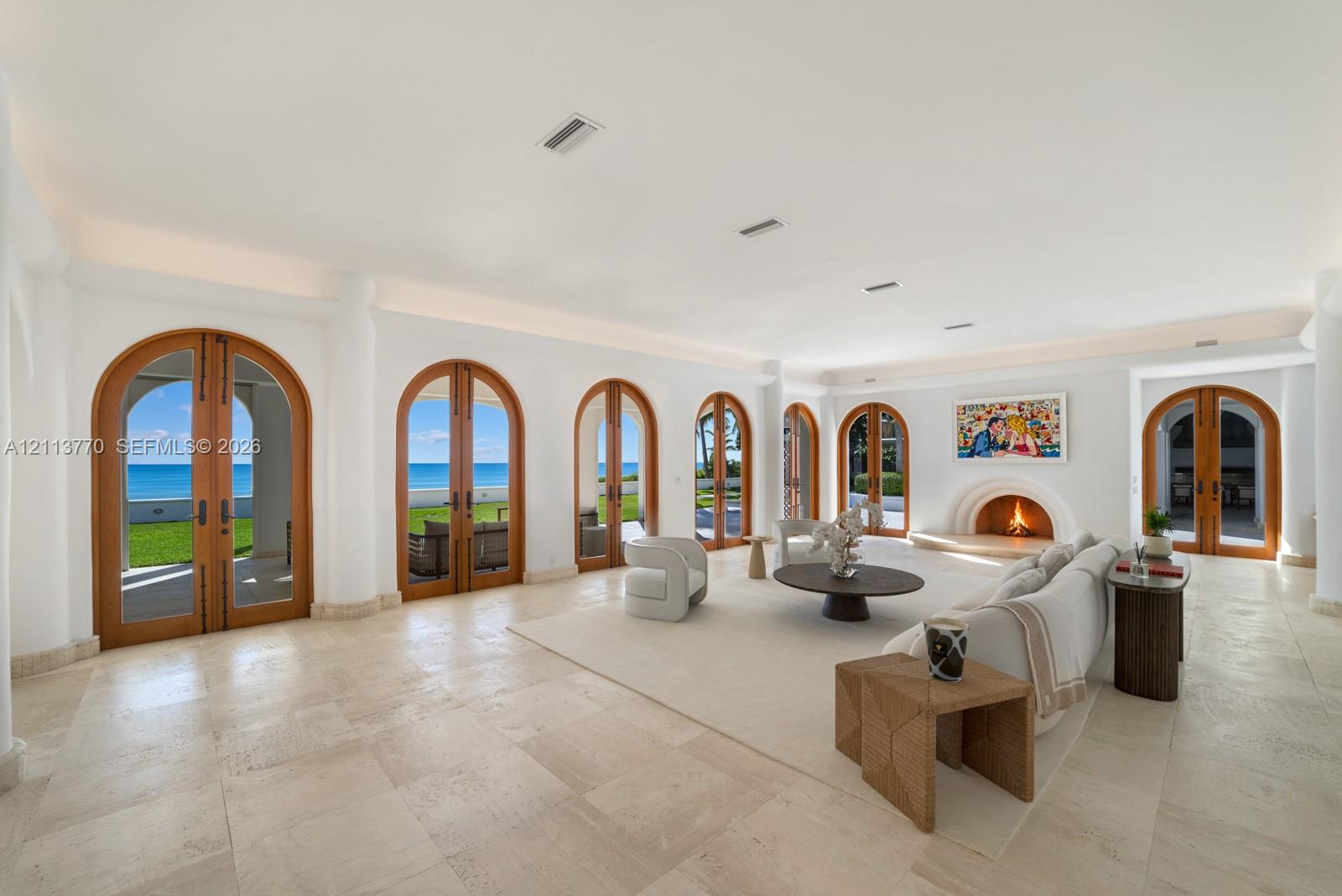 Living space featuring large-format stone flooring, multiple arched wood-frame glass doors, built-in recessed cove lighting, and an arched masonry fireplace