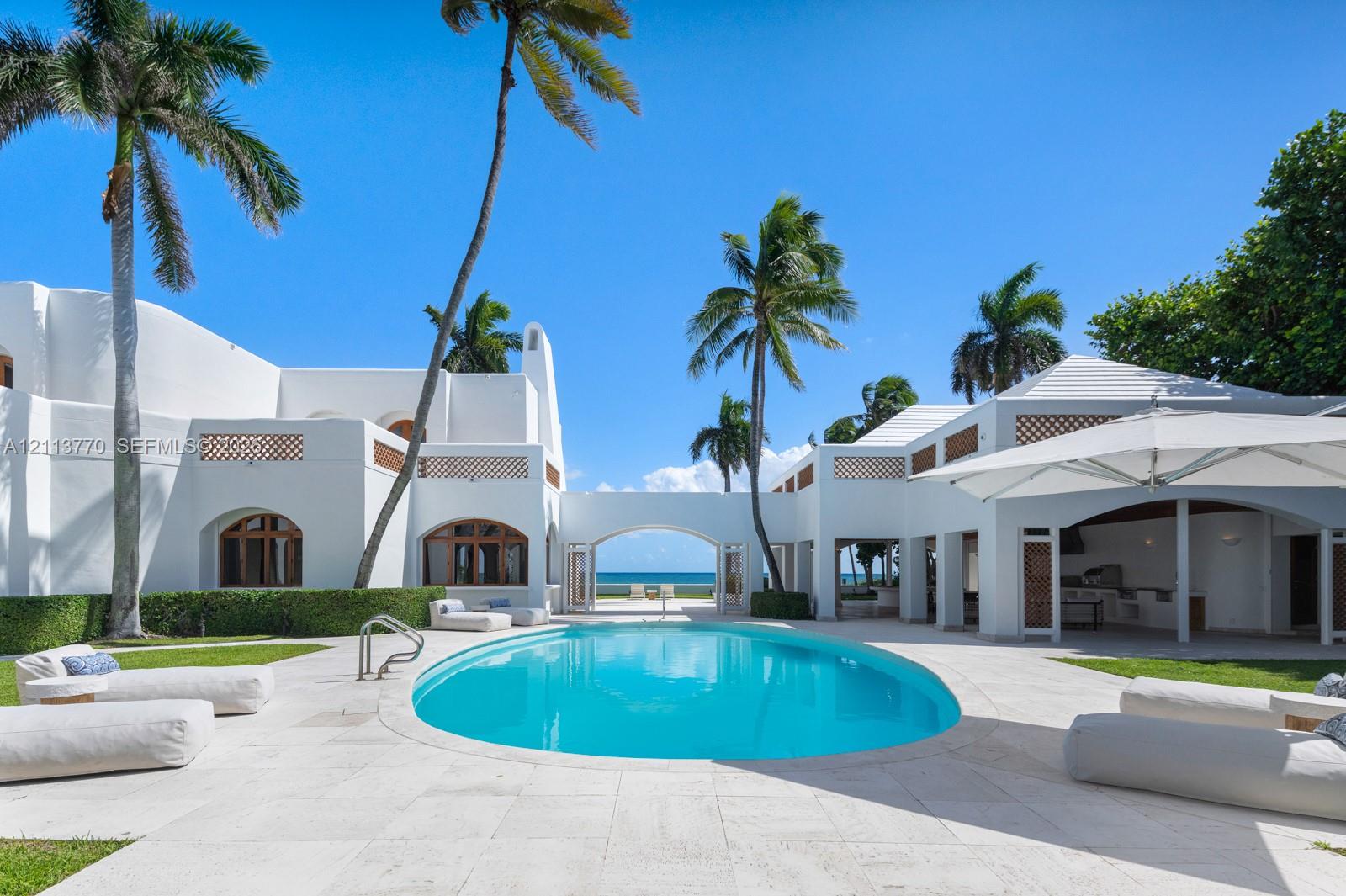 Exterior courtyard featuring an oval swimming pool, stone paved decking, stucco architecture with lattice accents, and an integrated outdoor kitchen