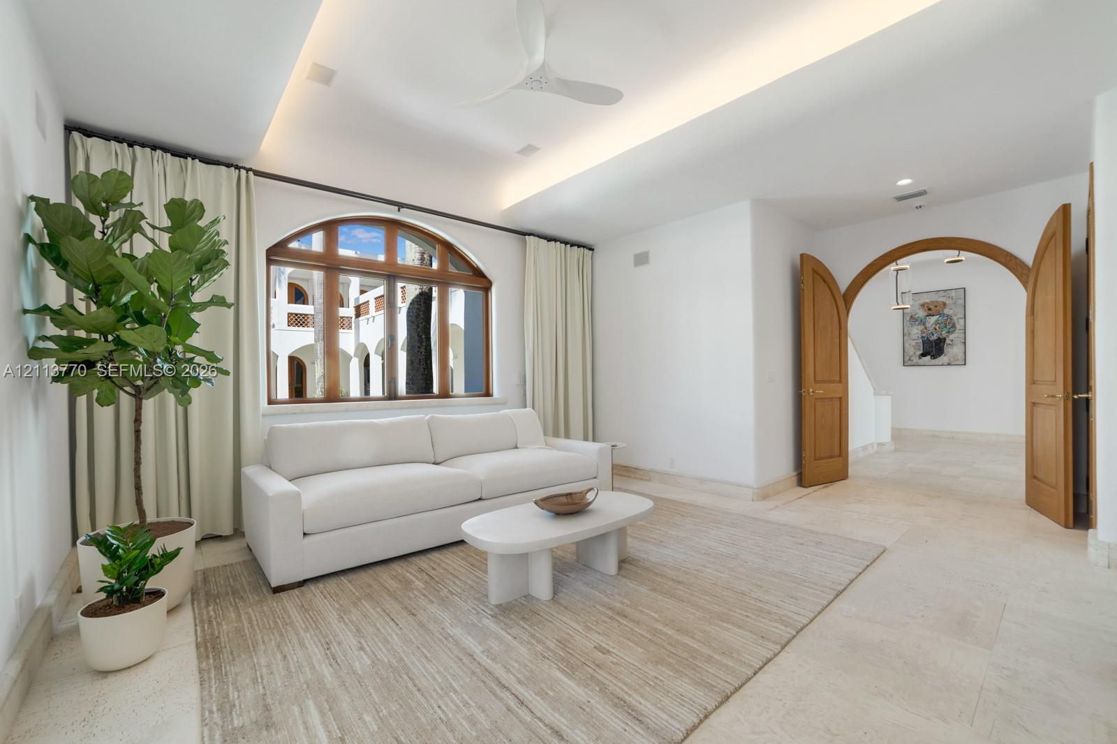 Tray ceiling with integrated recessed lighting, arched wood-framed window, natural stone tile flooring, and double wood-paneled arched doorway