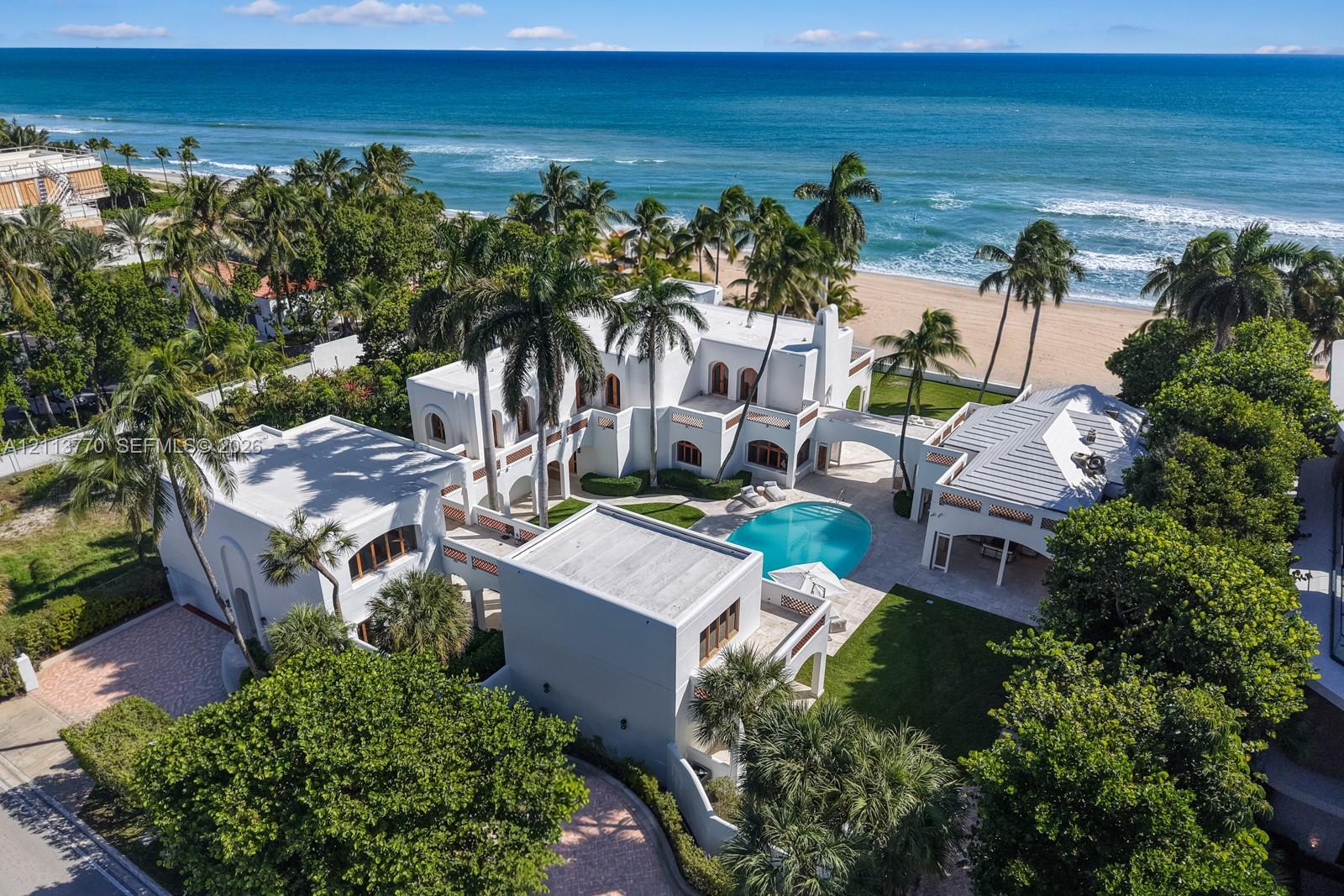 Coastal estate featuring a white stucco exterior, swimming pool, manicured lawn, stone-paved patio, and direct beach access