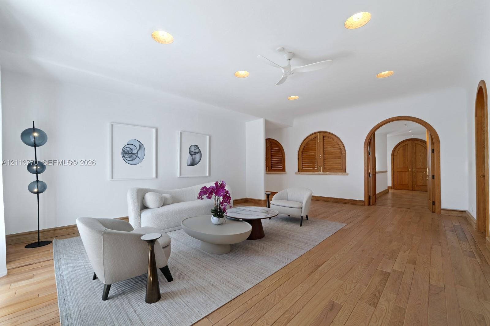 Living space featuring wood-finish flooring, recessed lighting, ceiling fan, arched doorways with wood trim, and arched window shutters