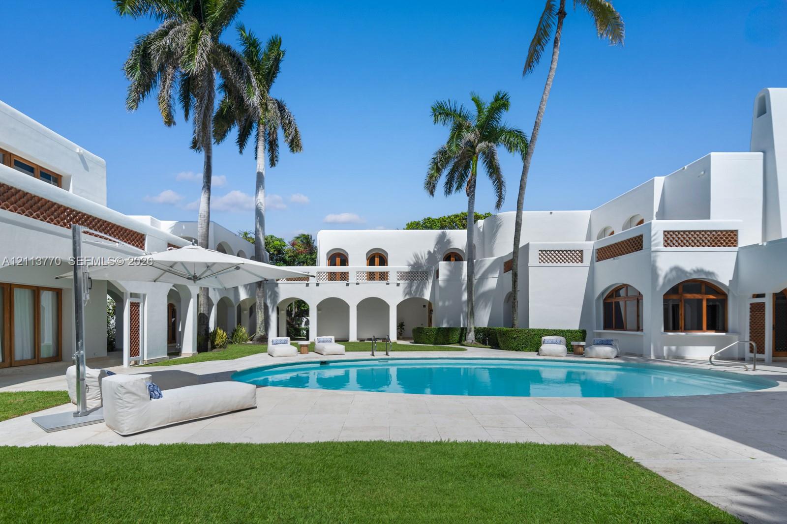 Courtyard featuring a curved swimming pool, stone patio, arched loggia, stucco exterior, and decorative lattice detailing