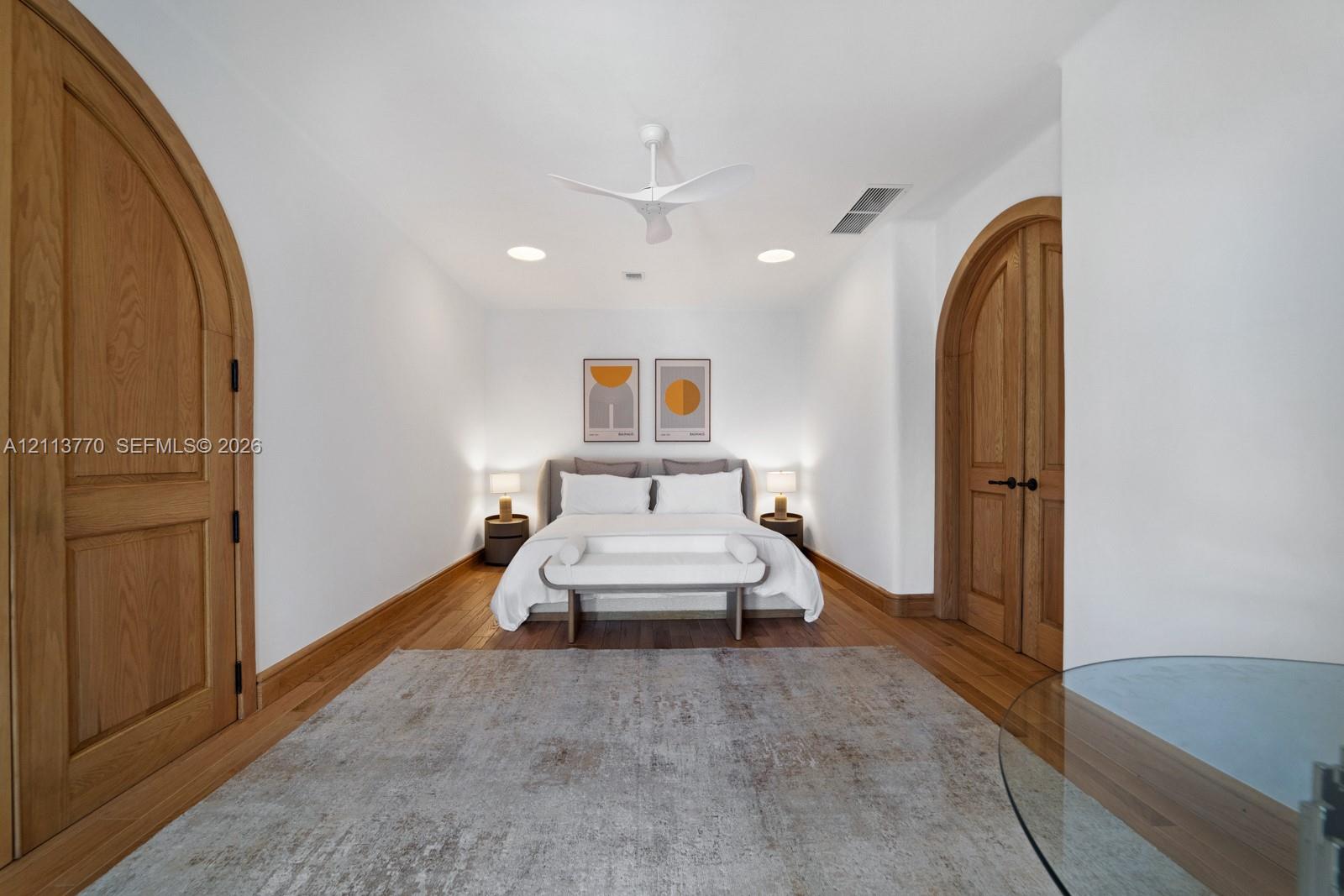 Interior room featuring arched solid wood doors, wood-finish flooring, and a modern white ceiling fan