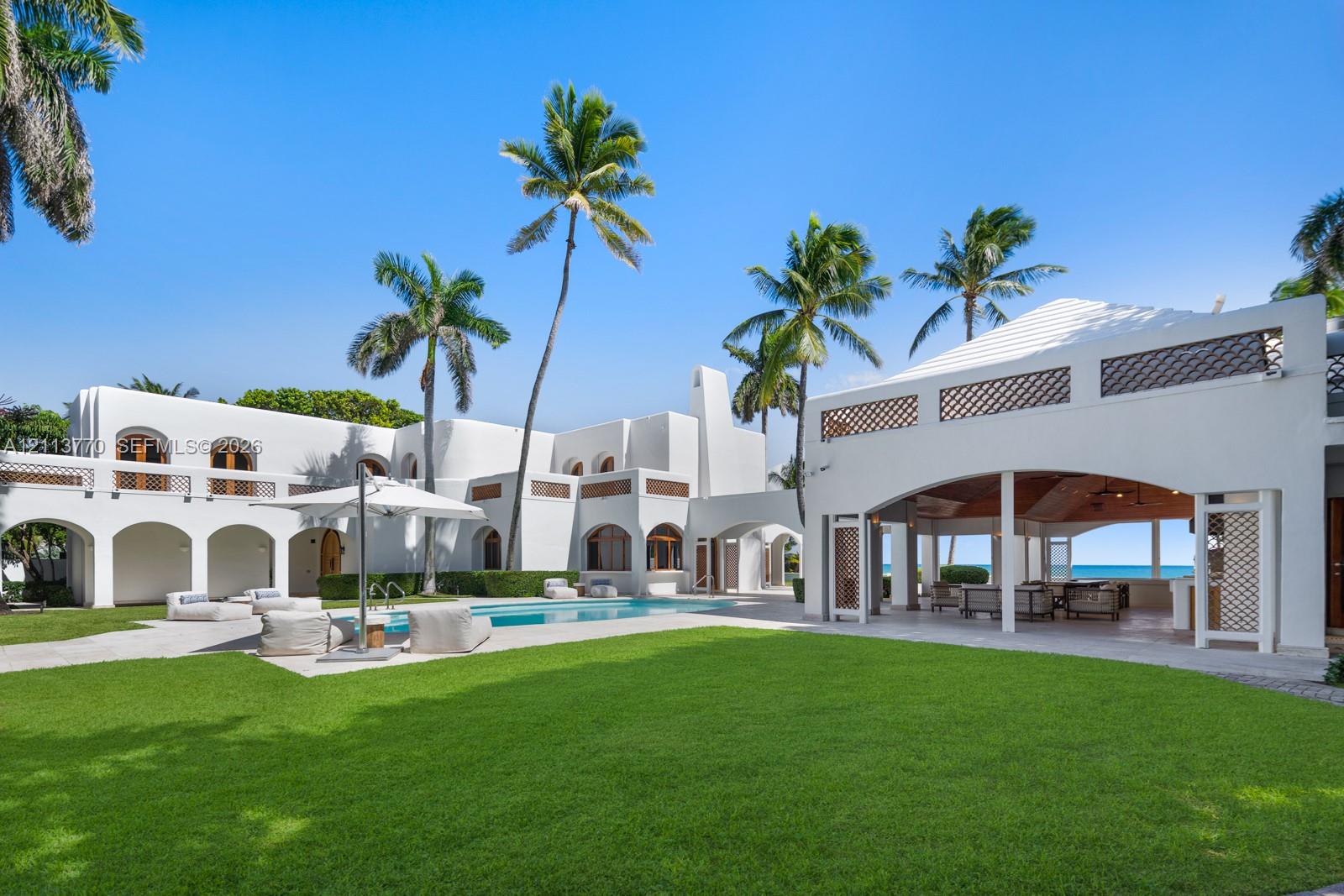 Stucco exterior with arched architectural detailing, expansive lawn, swimming pool with stone surround, and covered lanai featuring an open-air design