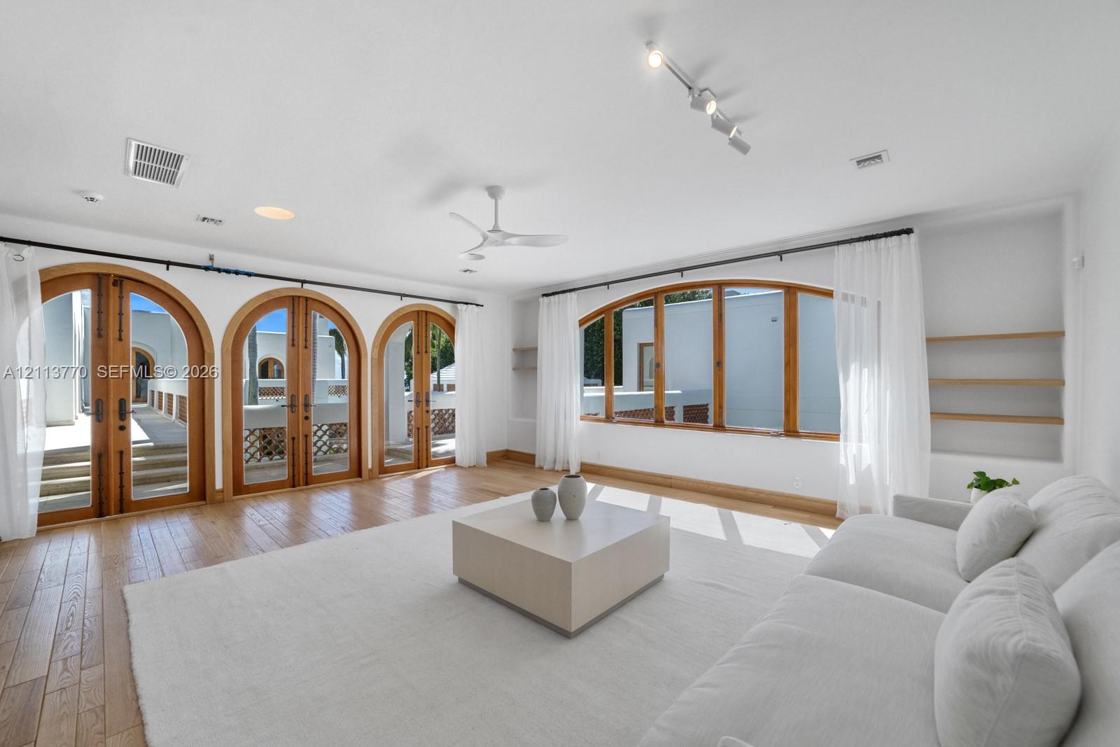Living space featuring arched wood-framed doors, wood-finish flooring, built-in wall shelving, a ceiling fan, and adjustable track lighting