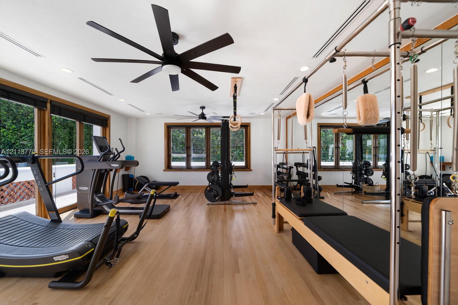Fitness space featuring wood-finish flooring, multi-blade ceiling fans, recessed lighting, expansive wall-to-wall mirrors, and wood-trimmed windows