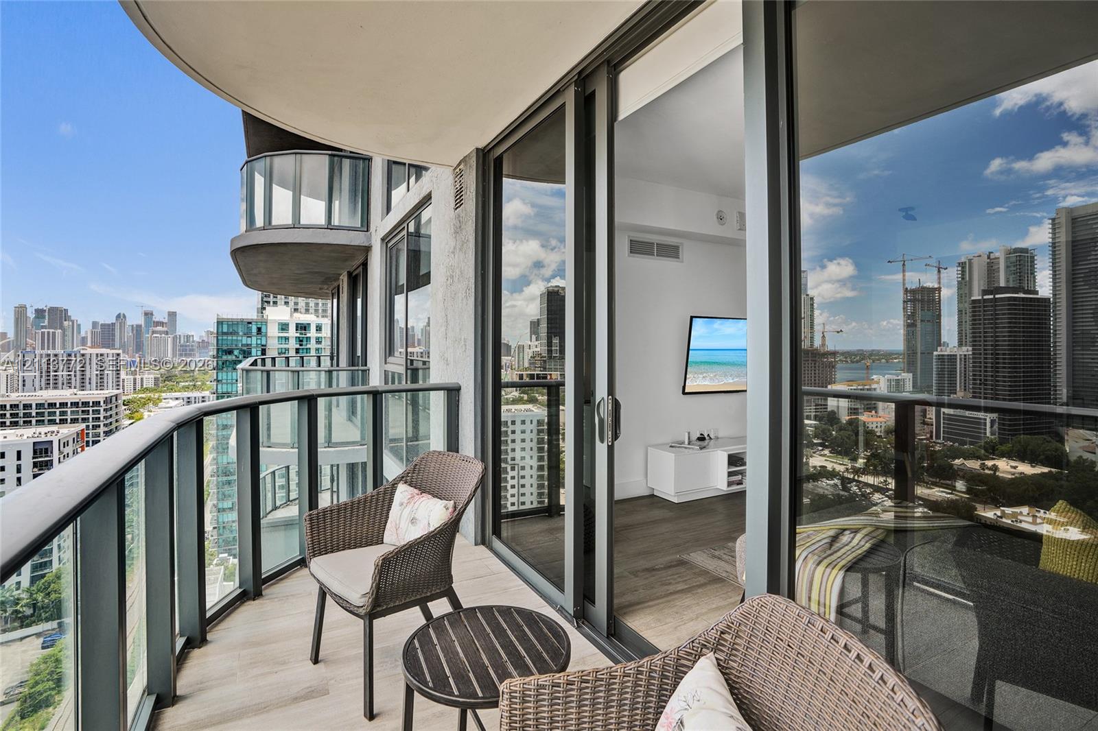 Private balcony with glass panel railing, wood-finish flooring, and floor-to-ceiling sliding glass doors