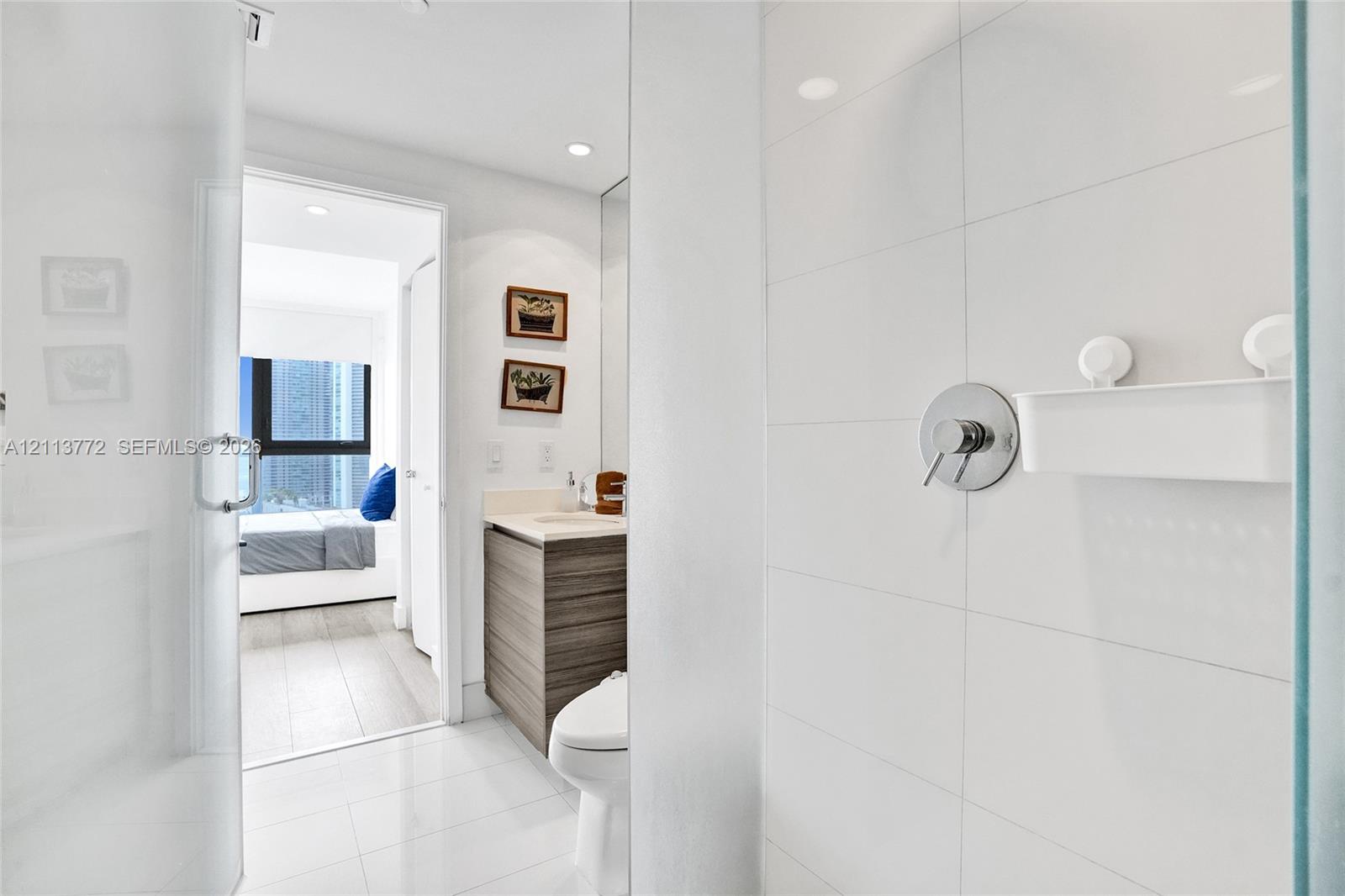 Full-height white tile shower enclosure featuring polished chrome fixtures, glass door, wood-finish cabinetry, and solid surface countertop