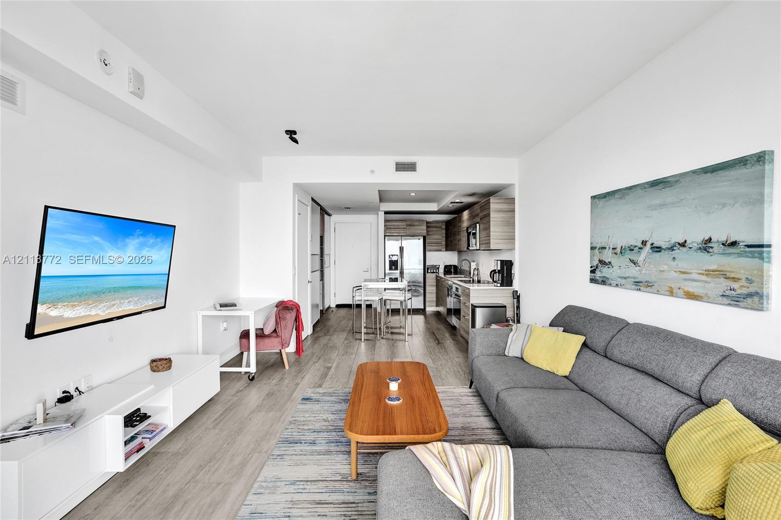 Open-concept interior featuring wood-finish flooring, kitchen with stainless steel appliances, flat-panel cabinetry, and integrated ceiling lighting