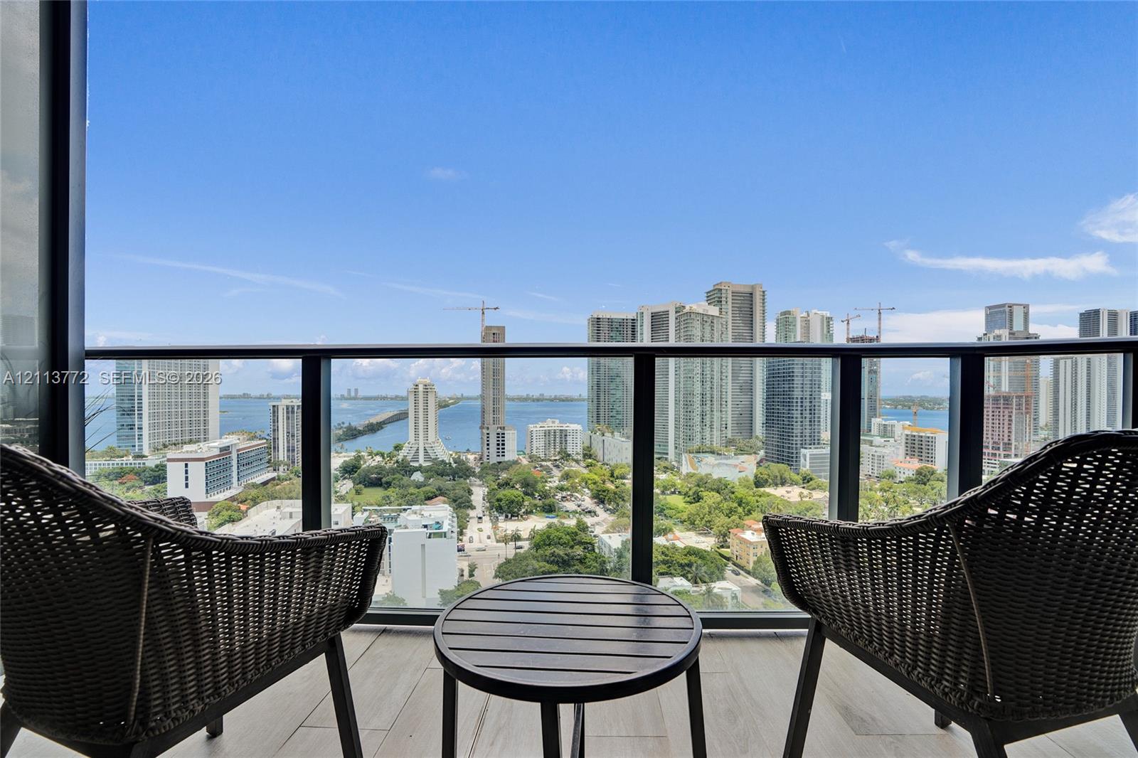 Covered balcony featuring tile flooring and a black metal railing with glass panels, providing an expansive metropolitan and waterfront panorama